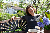 Frau entspannt auf Bank im Garten