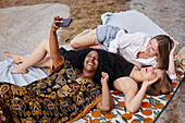 Drei Freunde, die auf einer Decke liegen und ein Selfie machen