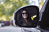 Smiling female driver reflecting in side mirror