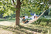 Mann liegt in einer Hängematte im Garten und benutzt ein Telefon