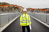 Porträt einer Ingenieurin in reflektierender Kleidung auf einer Brücke stehend
