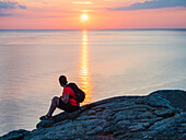 Woman sitting on rock and looking at sunset over sea