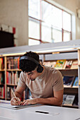 Männlicher Student macht sich in der Bibliothek Notizen