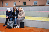 School friends sitting in front of school and using laptop