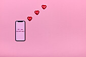 Smartphone and heart-shaped candies on pink background