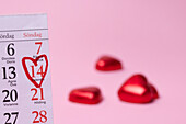 Heart-shaped candies and calendar on pink background