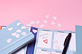 Herzförmiges Konfetti und Kalender auf rosa Hintergrund