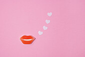 Rote Lippen und Papierherzen auf rosa Hintergrund
