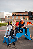 Portrait of teenage friends sitting in front of school