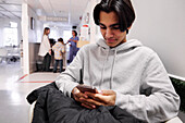 Young male patient waiting in outpatient clinic and using smart phone
