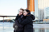 Junge Frauen, die im Winter am Fluss stehen und sich umarmen