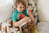 Boy holding newborn sibling and doing peace sign