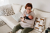 Großmutter füttert neugeborenen Enkel im Wohnzimmer
