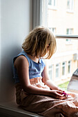 Blondes Mädchen schaut durch ein Fenster