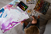 Boy sitting on floor and painting with watercolors