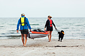 Couple carrying kayak at sea
