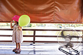 Girl holding balloon next to electric fan