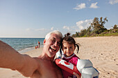 Portrait of grandfather taking selfie with granddaughter on beach