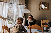 Grandmother and adult granddaughter sitting at table and having tea