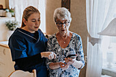 Hauspflegerin hilft Seniorin bei der Benutzung des Smartphones