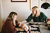 Lächelnde Mütter entspannen sich zu Hause mit neugeborenem Baby