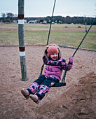 Girl in pink winter clothes swinging on swing