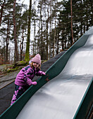 Girl in pink winter clothes climbing up slide