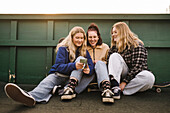 Teenager-Mädchen sitzen auf Skateboards und benutzen ein Smartphone