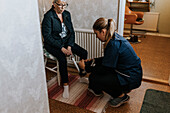 Hauspflegerin hilft Seniorin beim Anziehen der Schuhe