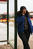 Frau, die an der Bushaltestelle mit ihrem Handy telefoniert