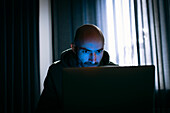 Mann arbeitet am Laptop in einem dunklen Büro