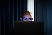 Mann arbeitet am Laptop in einem dunklen Büro