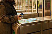 Frau, die mit ihrem Smartphone eine Fahrkarte für die U-Bahn bezahlt