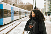Frau am Bahnsteig mit Handy in der Hand