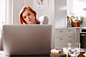 Frau hält sich den Nacken, während sie einen Laptop benutzt