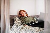 Schlafende Frau im Bett mit Laptop auf dem Schoß