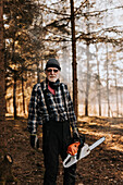 Senior man in forest holding chainsaw
