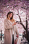 Junge Frau, die unter einer Kirschblüte steht und telefoniert