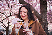 Junge Frau, die unter einer Kirschblüte steht und einen Zweig hält