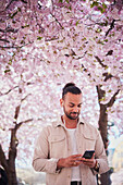 Junger Mann, der unter einer Kirschblüte steht und telefoniert