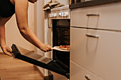 Mid section of woman taking pizza out of oven