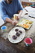 Man sitting at table and having fruit and cupcakes