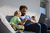 Vater sitzt mit seinen Söhnen an Deck und arbeitet an seinem Laptop