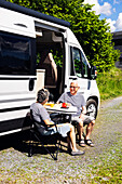 Älteres Paar sitzt vor einem Wohnwagen