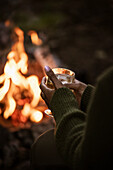 Woman holding glass of wine by campfire