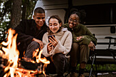 Friends sitting by campfire and using phone