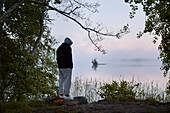 Man standing on lake shore at dusk