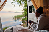 Junge Frau entspannt im Wohnmobil mit Blick auf den See