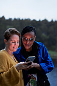 Lächelndes weibliches Paar benutzt Smartphone im Freien