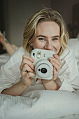 Blond woman photographing in bedroom